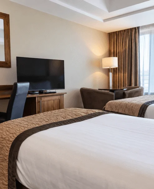 Elegant hotel room with twin beds, cosy seating, and natural light streaming through large windows.