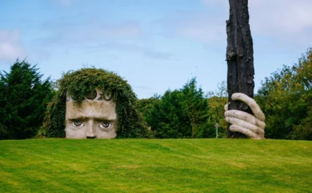 Sculpted face in lush garden with greenery and trees