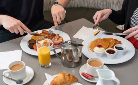 A couple enjoying a hearty breakfast in a cosy hotel setting with coffee and orange juice.