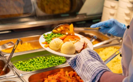 Chef serving a warm meal with vegetables in a hotel buffet setting.