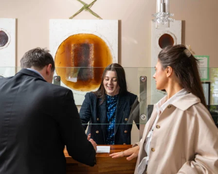Couple checking in at hotel reception with friendly staff in a warm, inviting lobby.