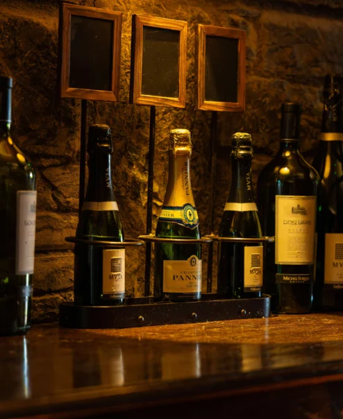 Assorted wine bottles on a warm, rustic wooden shelf in a cosy, inviting atmosphere.