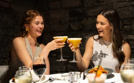 Two women enjoying cocktails and smiling in a cosy restaurant setting.
