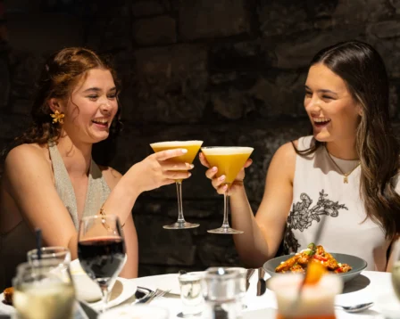 Two women enjoying cocktails and smiling in a cosy restaurant setting.
