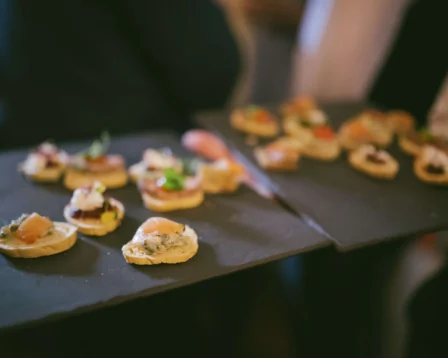 A group enjoying gourmet canapés on slate trays at a warm, elegant gathering.