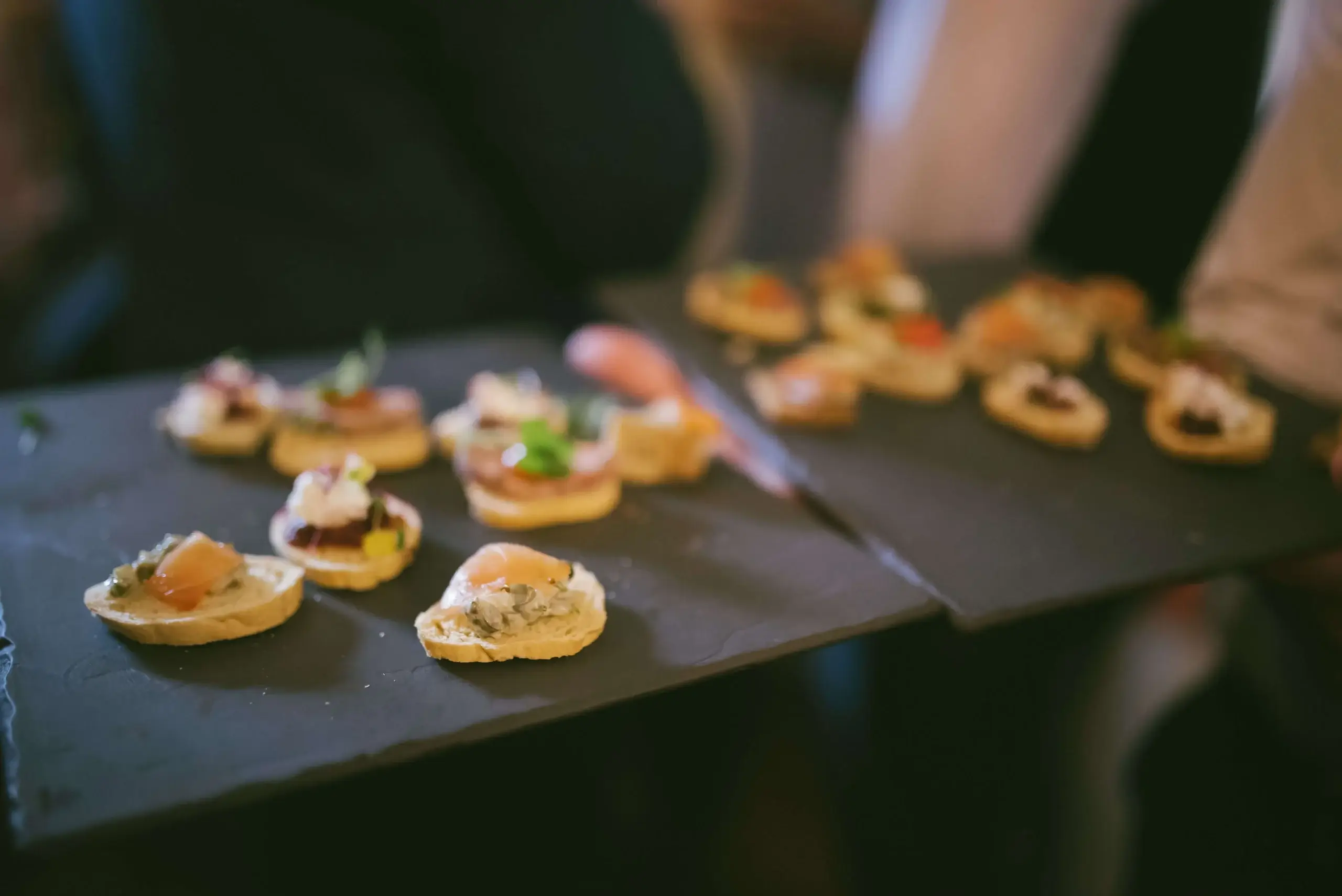 A warm gathering with people sharing artisanal canapés on slate boards.