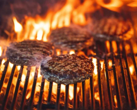 Juicy burgers sizzling on a hot grill with vibrant flames.