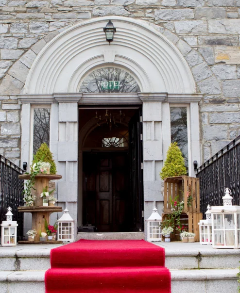 Elegant hotel entrance with red carpet, lanterns, and stone facade.
