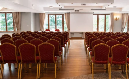 Elegant hotel conference room with rows of red chairs facing a projector screen.