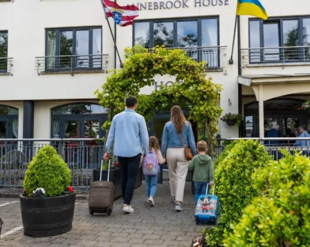 Family entering a charming hotel with suitcases under vine-covered archway.