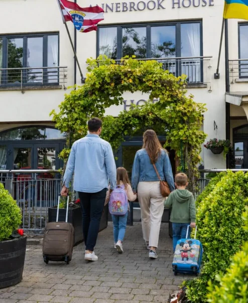 Family entering a charming hotel with suitcases under vine-covered archway.
