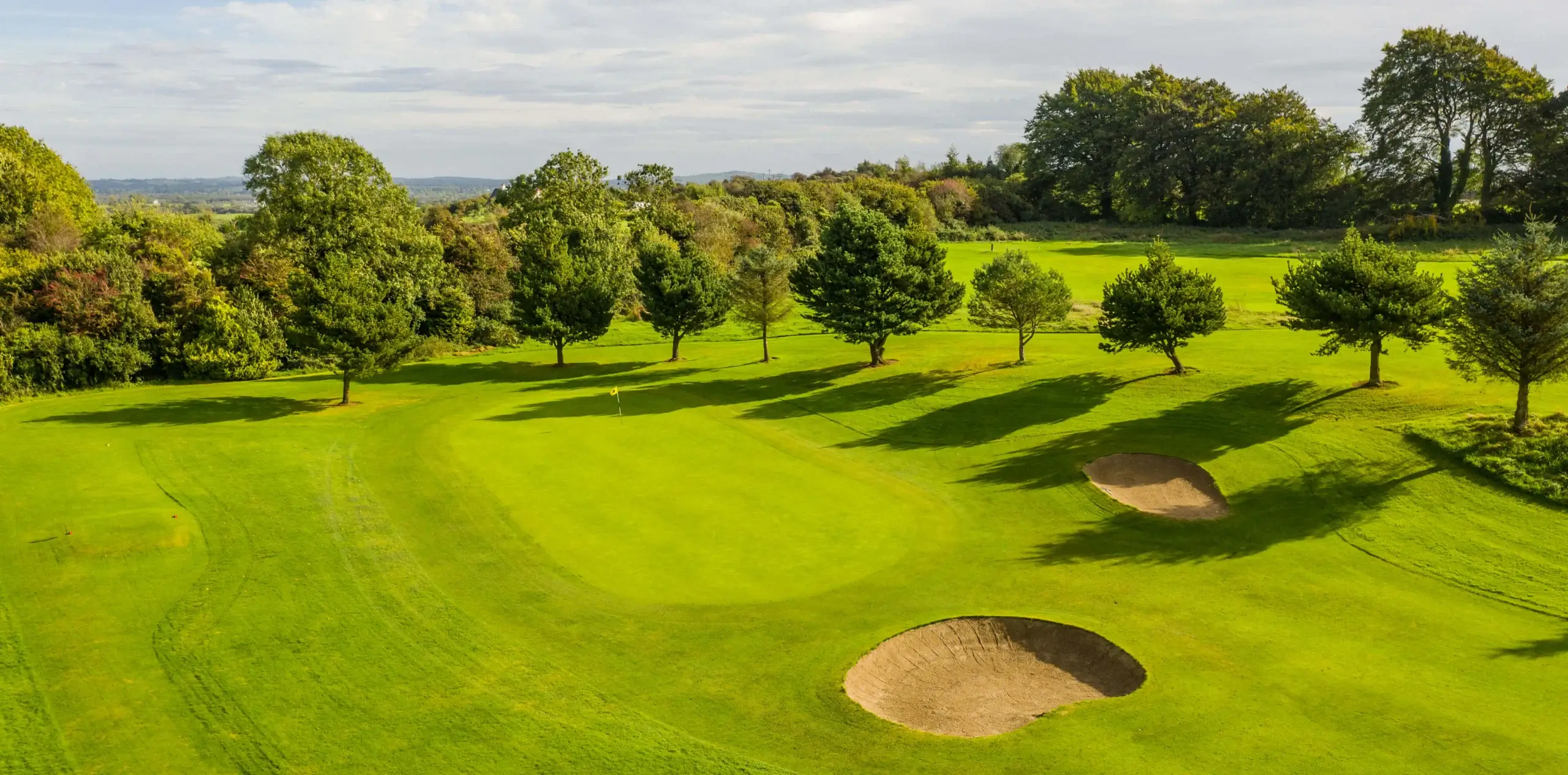 Picturesque golf course with lush greenery and sand bunkers under a clear sky.