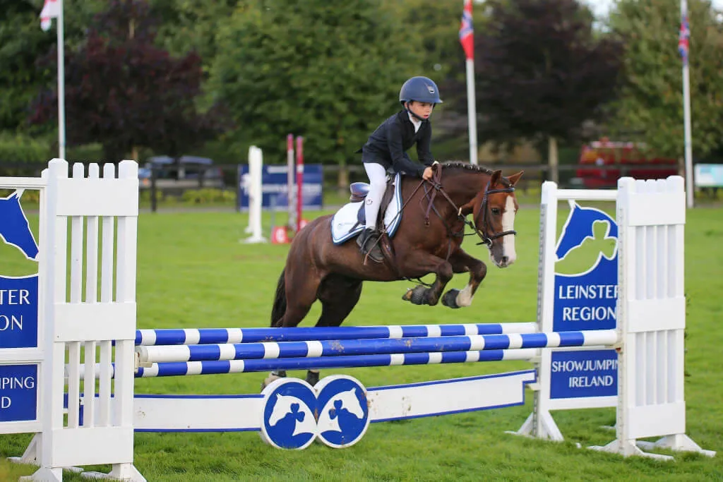 A young rider jumping a horse over a fence in an outdoor equestrian event.