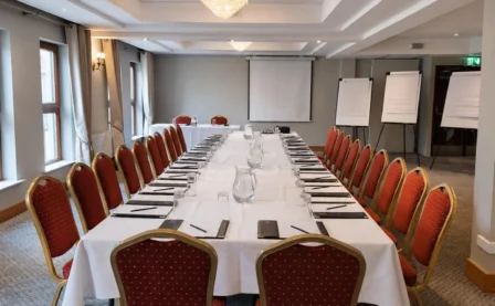 Elegant hotel conference room set for meetings with a large table and red chairs.