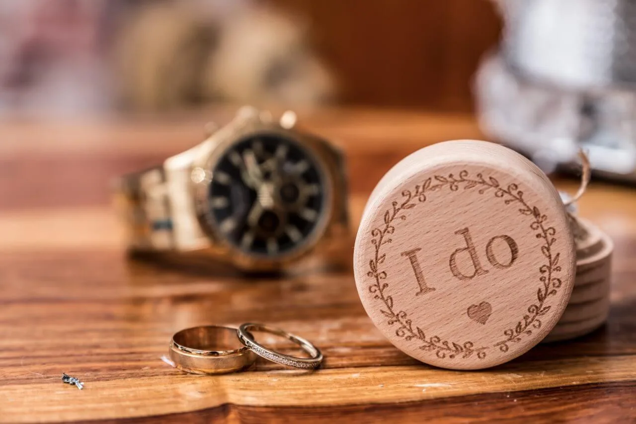 Wooden "I do" disc with wedding rings on a table, symbolising a romantic commitment.