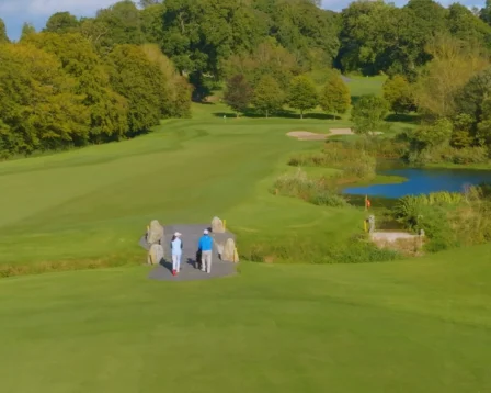 Family enjoying a scenic walk on a lush golf course beside a tranquil pond.