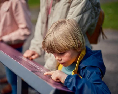 A young child points at a sign outdoors with family nearby.