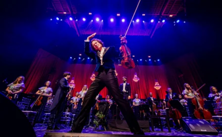 A lively orchestra performance with a passionate violinist, surrounded by bright stage lights.