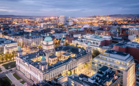 Aerial view of a lively cityscape at dusk, showcasing illuminated historic and modern buildings.