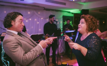 A joyful couple dancing at a lively hotel event with live band in the background.