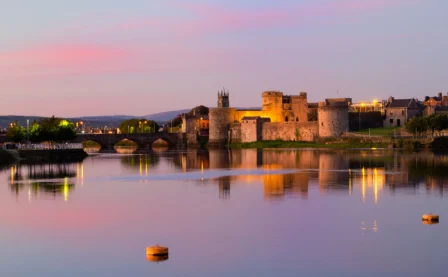 Tranquil evening view of a historic riverside castle with warm lights and serene reflections.