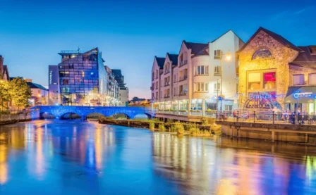 A picturesque riverside view of a lively hotel district at dusk, featuring glowing lights and reflections.