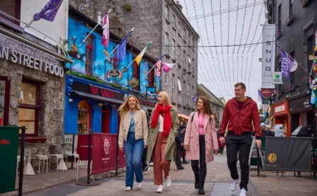 A cheerful group strolls through a vibrant, bustling street lined with colourful buildings and eateries.