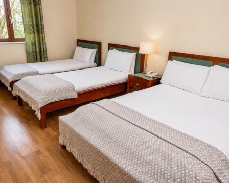 Cosy hotel room with three inviting beds, a bedside lamp, and a window view.