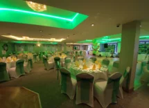 Elegant dining space set for a hospitality event with green lighting and decorated tables.