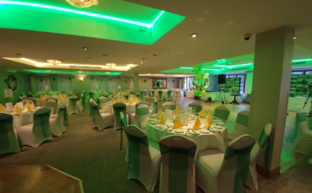 Elegant dining space set for a hospitality event with green lighting and decorated tables.