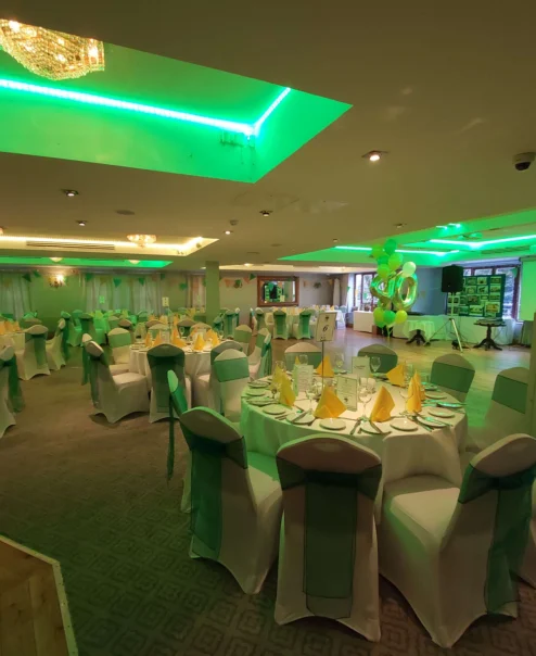 Elegant dining space set for a hospitality event with green lighting and decorated tables.