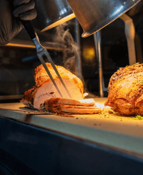 Chef carving roasted meat in a warm, inviting restaurant kitchen.
