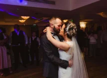 A joyful couple shares a first dance at a warmly lit wedding reception, surrounded by family.