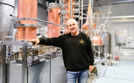 Man smiling in a modern brewery setting with copper equipment.