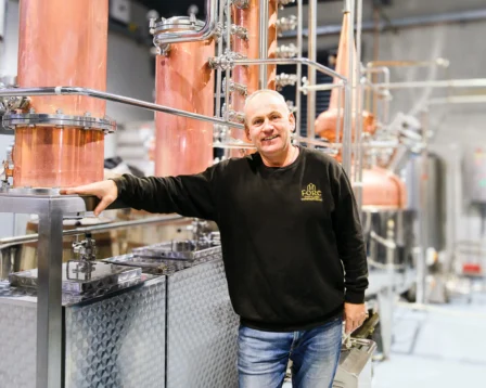 Man smiling in a modern brewery setting with copper equipment.