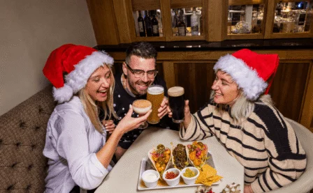 A cheerful group wearing Santa hats enjoying drinks and appetisers in a cosy restaurant.