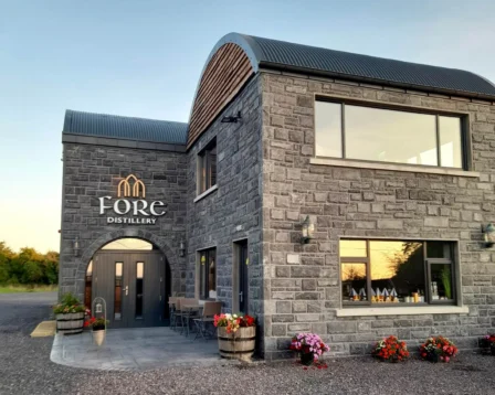 Modern stone distillery at sunset with flowers and a welcoming entrance.