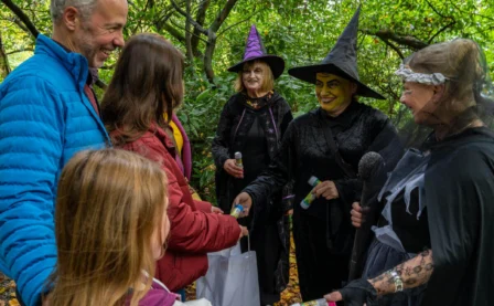 A family enjoys a Halloween event with people in witch costumes at a forested resort.