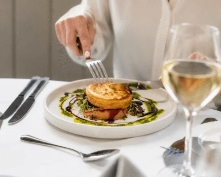 A woman enjoying a gourmet meal with wine at a cosy restaurant.