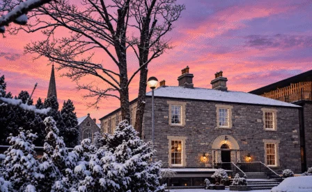 A historic stone hotel warmly lit at sunset, surrounded by snow, welcoming guests in winter.
