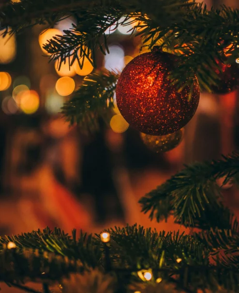 Festive Christmas tree with a red bauble in a cosy, warmly lit hotel lobby.