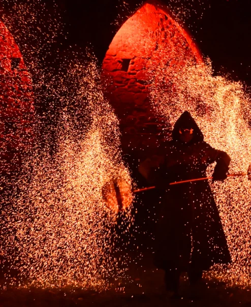 Family enjoying a night fire‑dance performance amid glowing sparks and stone arch backdrop