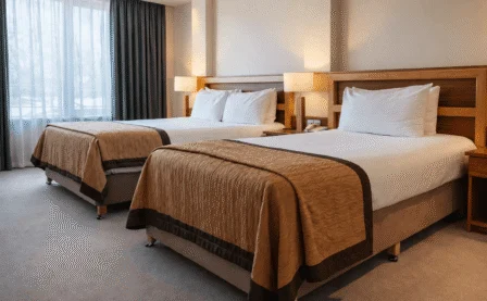 Spacious hotel twin room with two made beds, warm lighting, family-friendly modern decor, window view