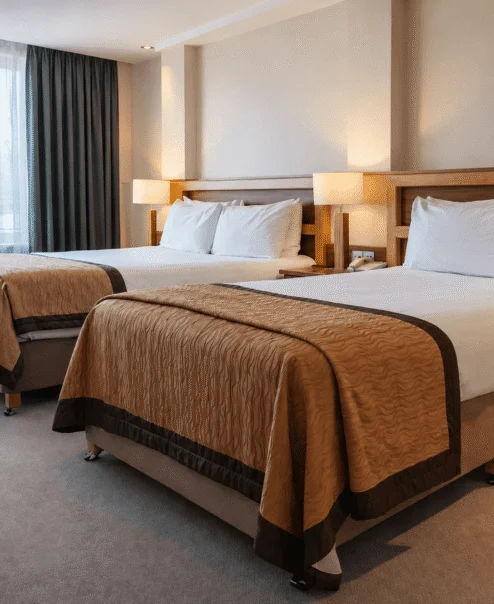 Spacious hotel twin room with two made beds, warm lighting, family-friendly modern decor, window view