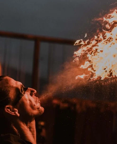 Family enjoying a fiery outdoor show as a performer breathes flame from a torch at dusk, lively resort entertainment