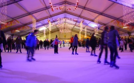 Families ice skating under festive lights in a cosy indoor rink.